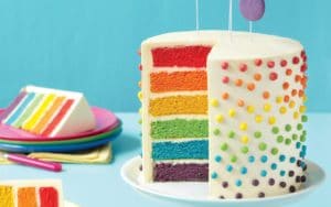 A frosted layer cake sliced open to reveal six layers in rainbow colors.